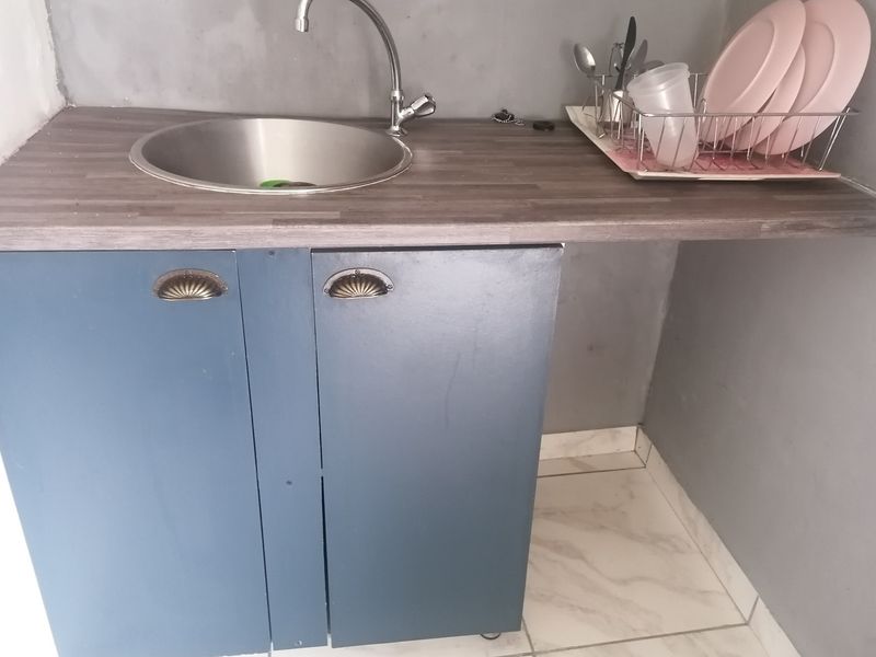 A compact scullery area featuring a stainless steel sink, laminate countertop, and blue built-in cabinetry with tiled flooring.