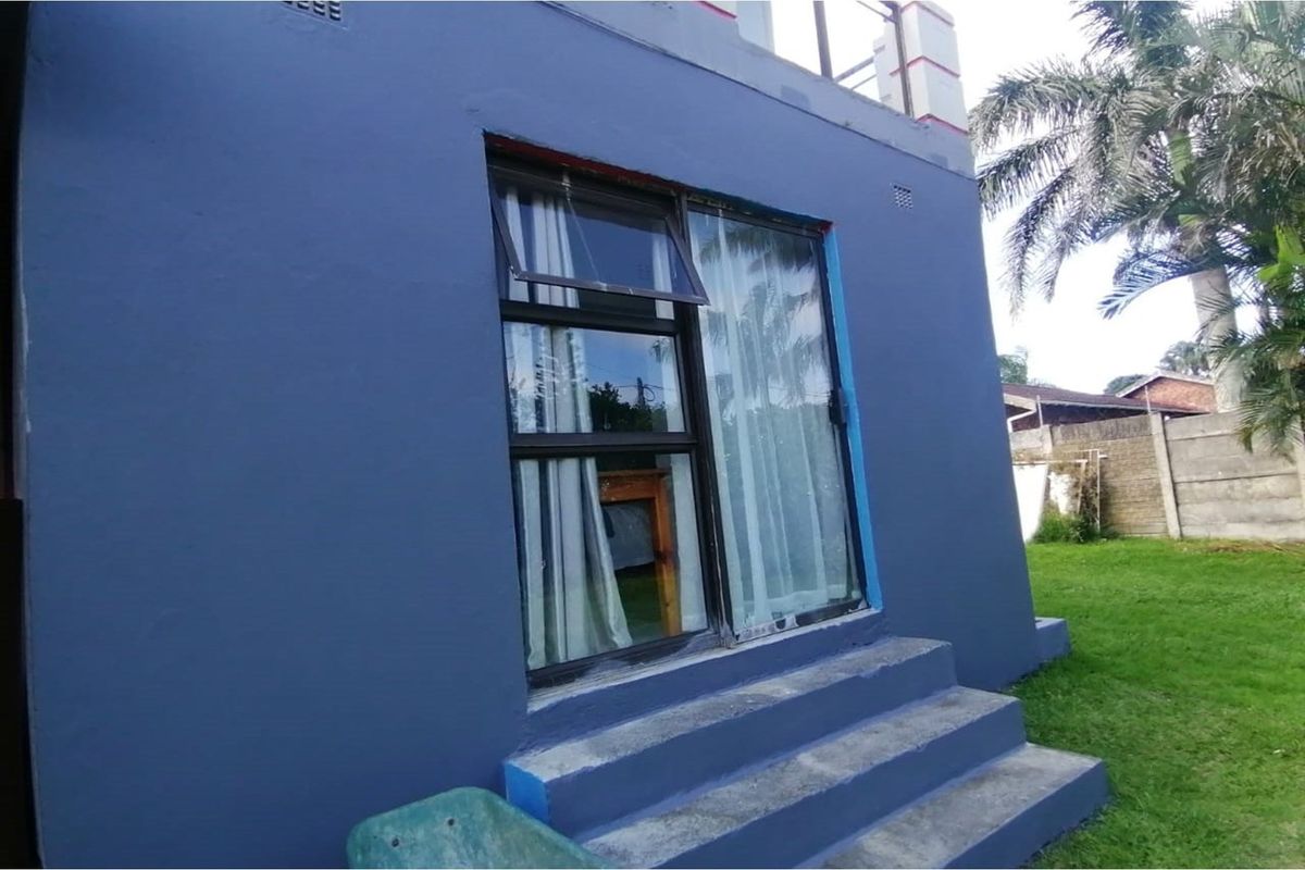Rear exterior view of the property featuring a sliding glass door, top-hung window, and concrete steps leading into the garden area.