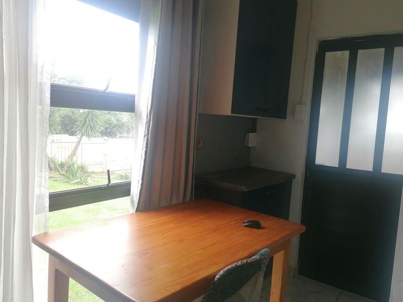 A small office or study area featuring built-in cabinetry, a large window with garden views, and a glass-panelled door.