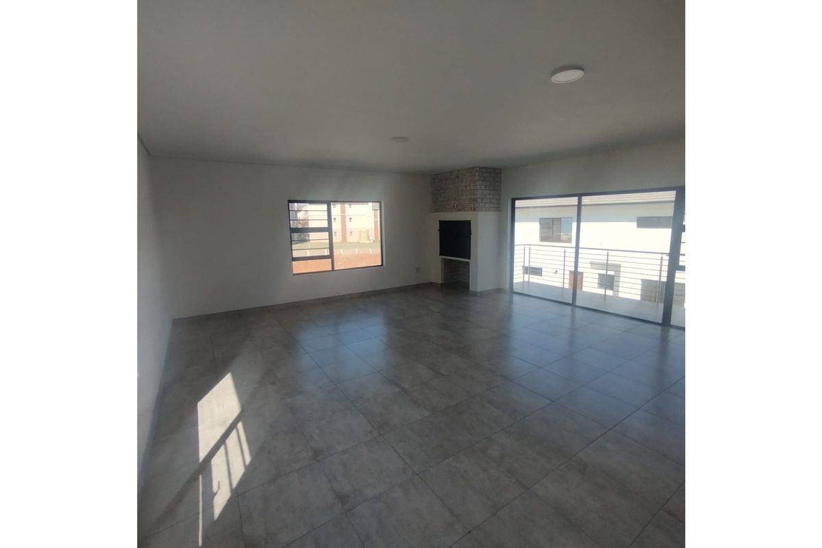 Spacious open-plan living area featuring large format floor tiles, a built-in brick fireplace, and sliding glass doors leading to a balcony.