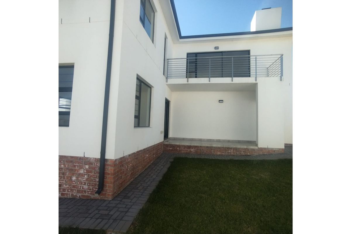 A view of the rear exterior of the house, featuring a covered patio area, a balcony with metal railings, and a paved walkway.