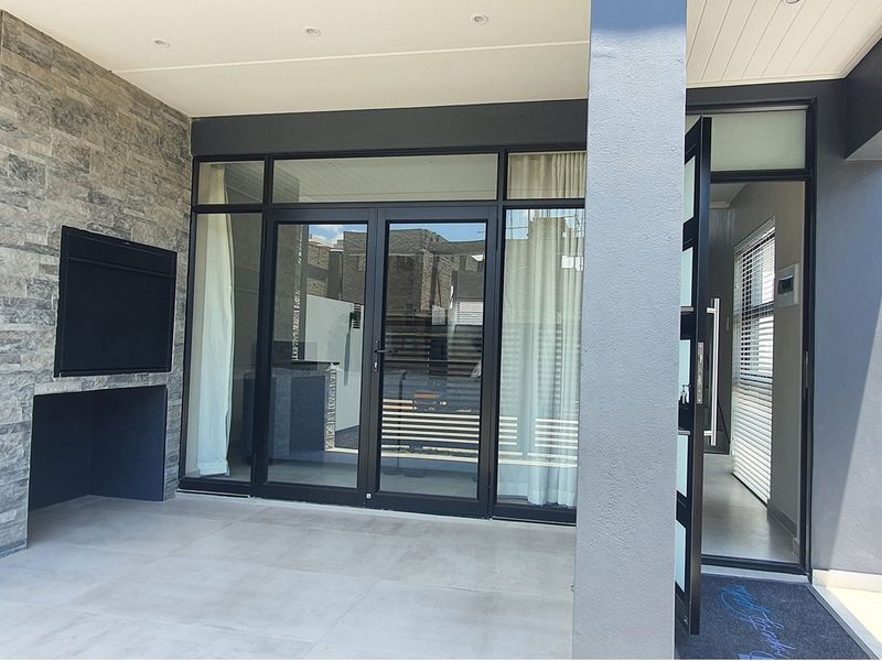 Covered patio area featuring a built-in braai with stone cladding, tiled flooring, and large glass sliding doors leading into the apartment interior.