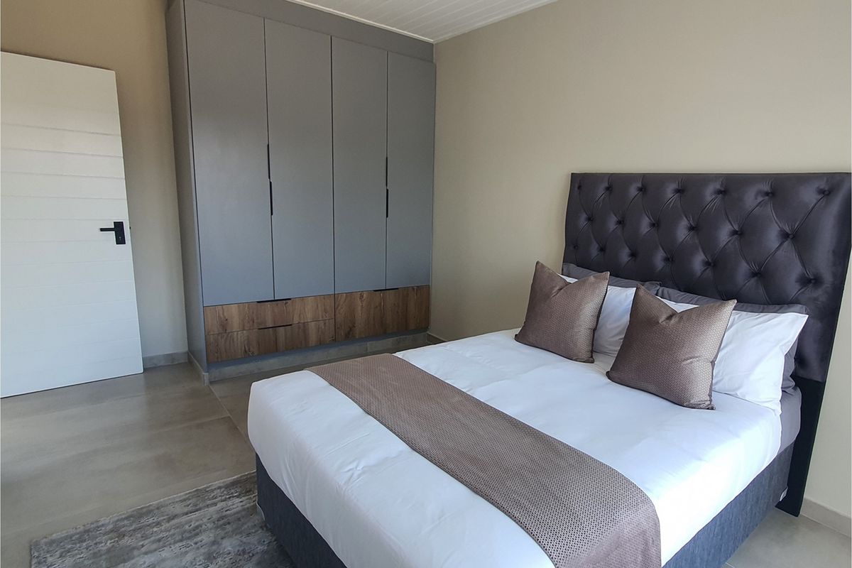 A modern bedroom featuring built-in grey and wood-tone cabinetry, neutral wall finishes, and tiled flooring.