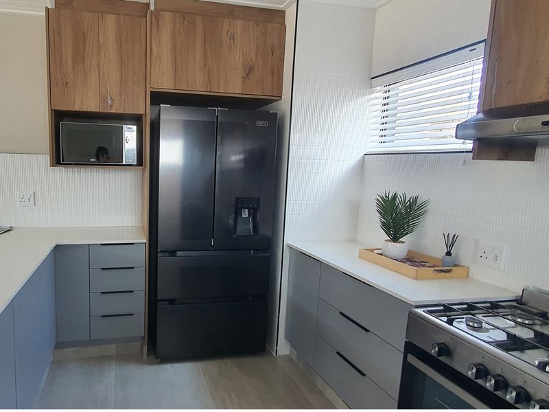 Modern kitchen featuring wood-grain upper cabinetry, grey lower cabinets, white stone countertops, and integrated stainless steel gas stove and extractor fan.