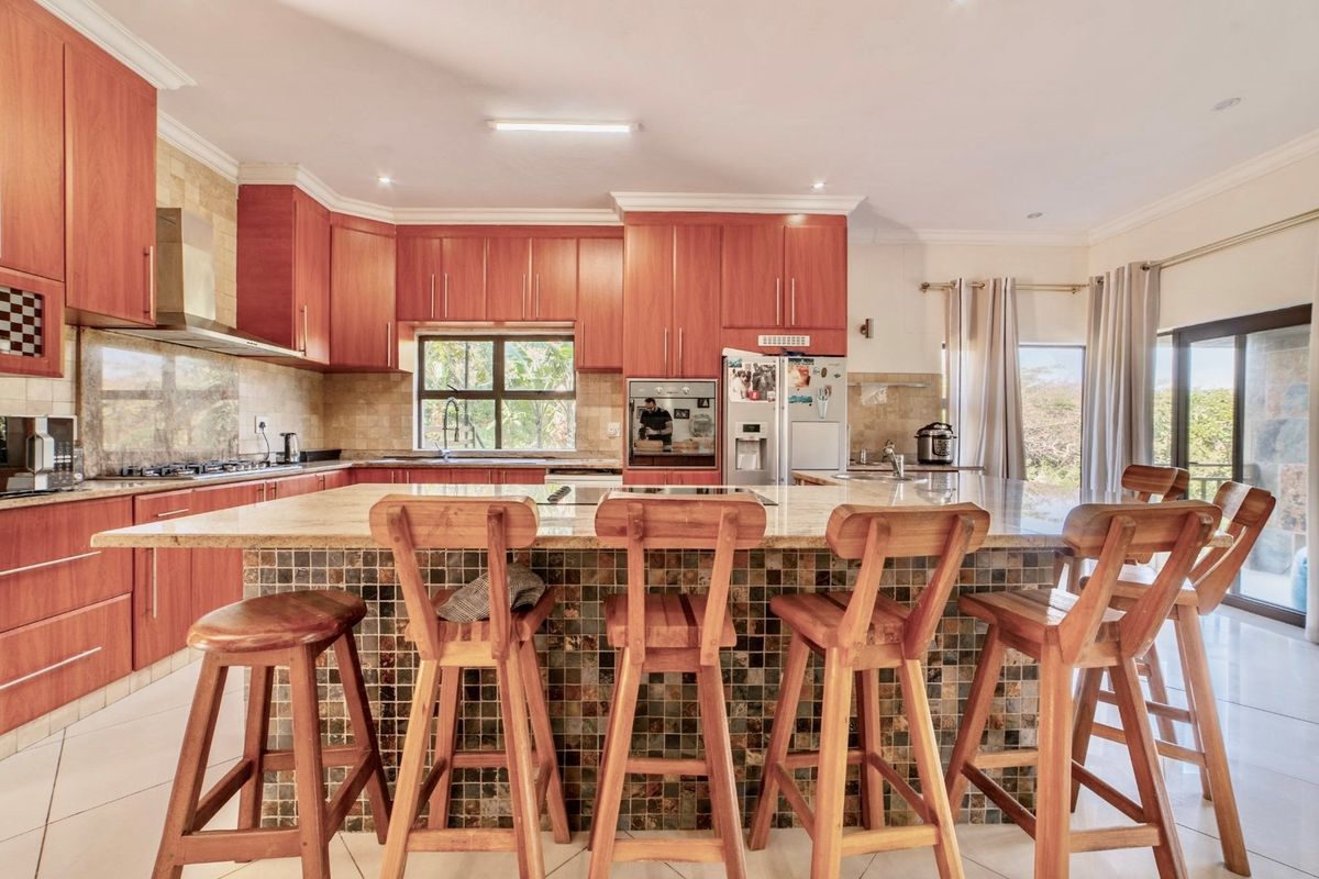 Spacious kitchen featuring wooden cabinetry, granite countertops, a large central island with mosaic tile detailing, and integrated appliances.