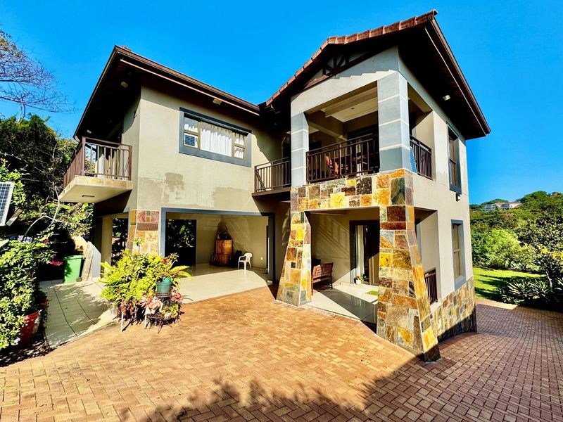 A two-story residential property featuring stone-clad pillars, multiple balconies, and a paved driveway area.