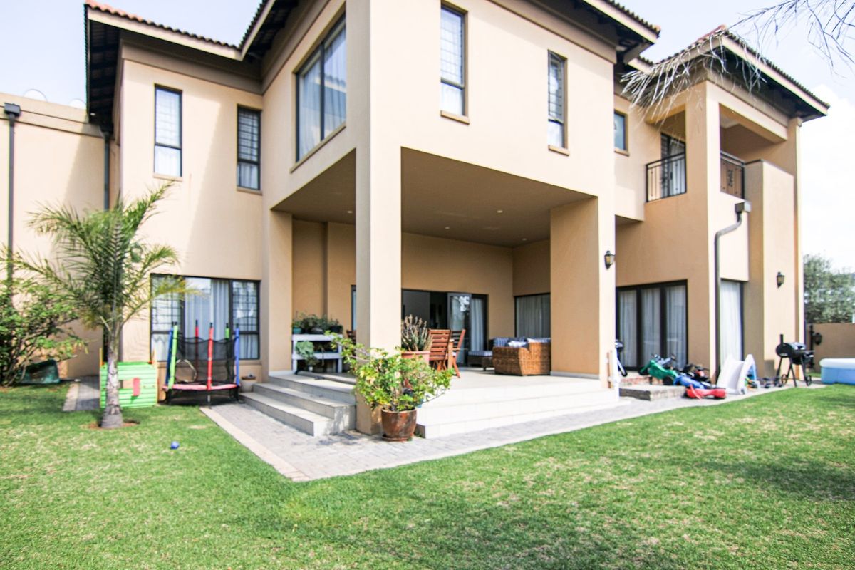 A spacious rear exterior view of a two-story house featuring a covered patio area, paved terrace, and a well-maintained garden.