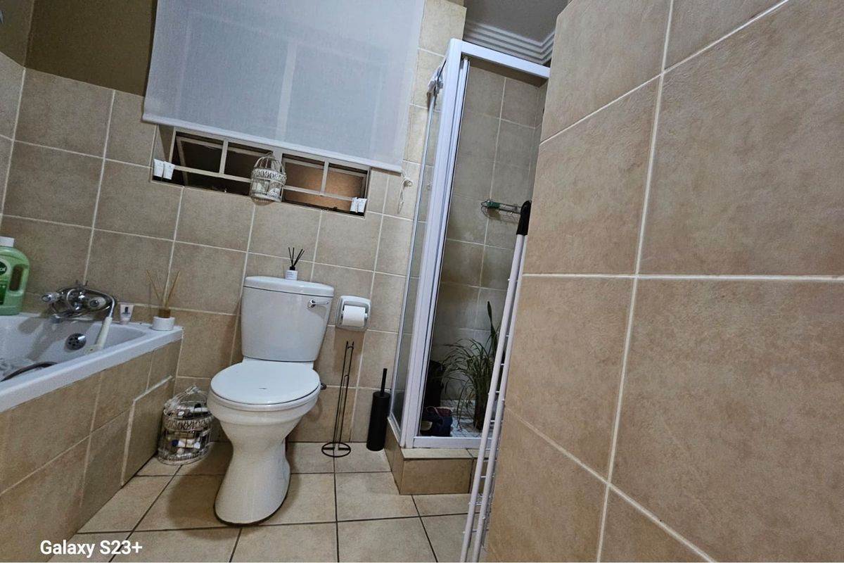A functional bathroom featuring a built-in bathtub, a separate glass-enclosed shower, and tiled walls and flooring throughout.