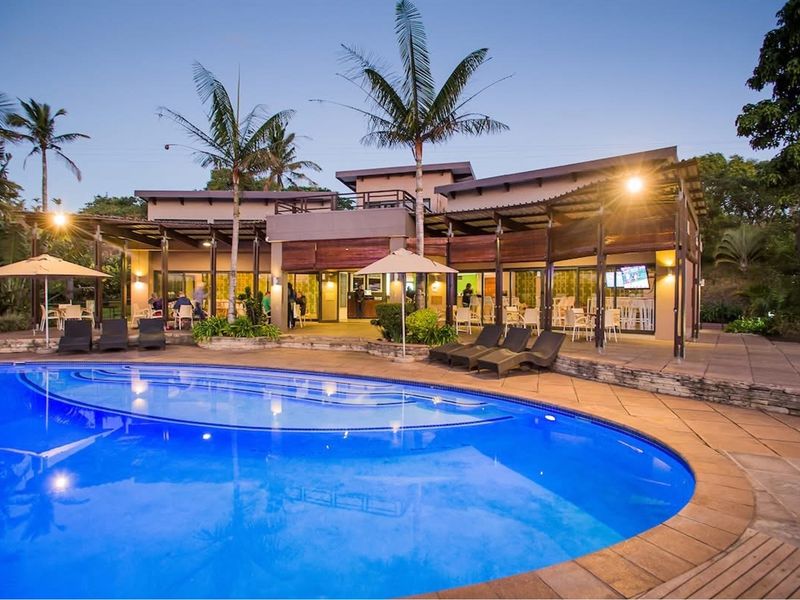 A well-maintained outdoor entertainment area featuring a large swimming pool, expansive stone-paved patio, and covered terrace with integrated lighting.