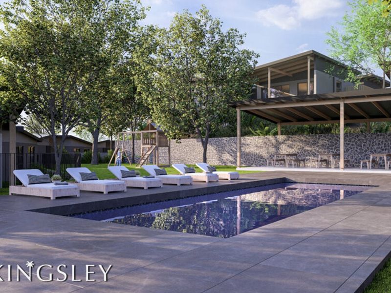 A modern outdoor pool area featuring a tiled deck, stone retaining wall, and a covered patio space within a landscaped garden setting.