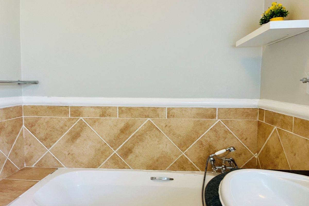 A bathroom featuring a bathtub with a handheld shower mixer, complemented by decorative beige wall tiling and a chair rail finish.
