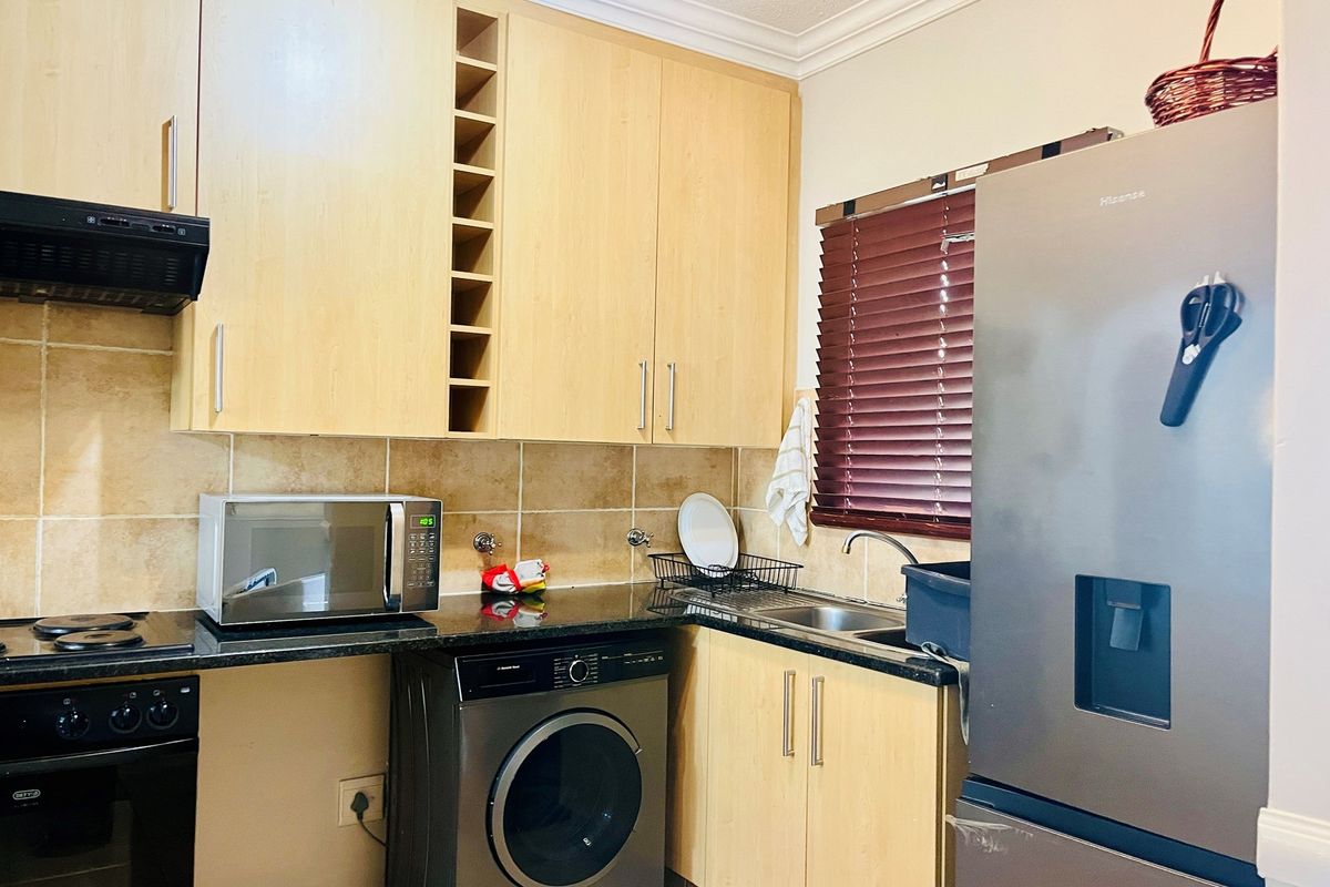 Compact kitchen featuring light wood cabinetry, dark granite countertops, tiled backsplash, built-in oven, hob, extractor fan, and integrated plumbing for a washing machine.