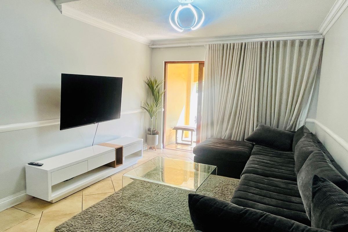 A comfortable living room featuring tiled flooring, crown molding, and direct access to an outdoor balcony area.