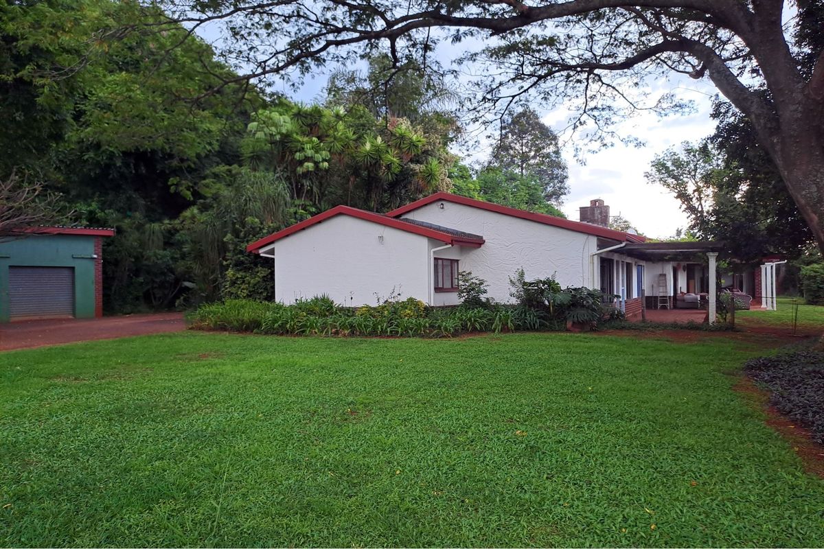 Rear view of the farm property featuring a white exterior, pitched roof, covered patio area, and a detached garage set within a large garden.