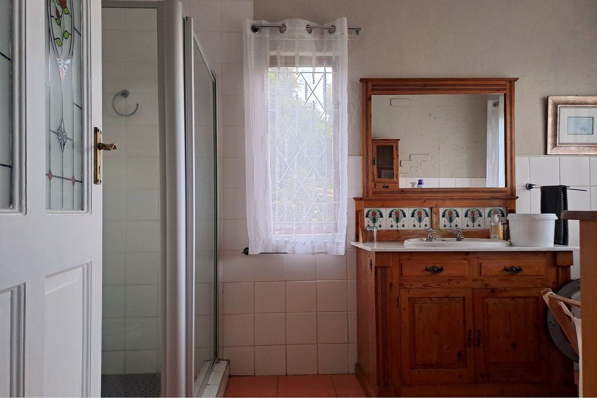 A functional bathroom featuring a shower enclosure, a wooden vanity cabinet with a tiled splashback, and a leaded glass window.