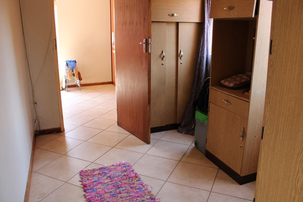 A bedroom featuring built-in wooden cupboards and neutral tiled flooring, providing functional storage and a clean, practical layout.