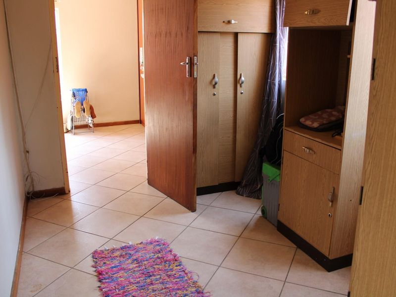 A bedroom featuring built-in wooden cupboards and neutral tiled flooring, providing functional storage and a clean, practical layout.