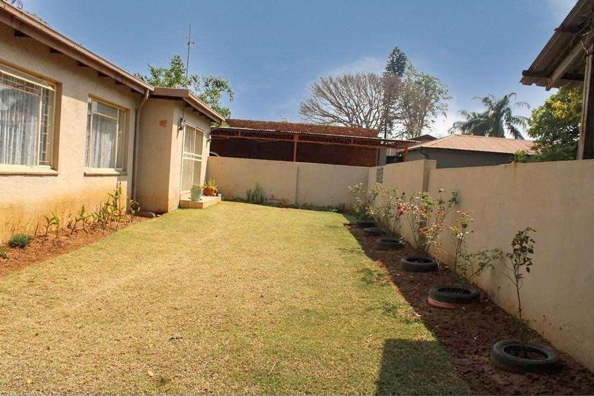 A rear garden area featuring a lawn, boundary wall, and access to the house via a sliding door.