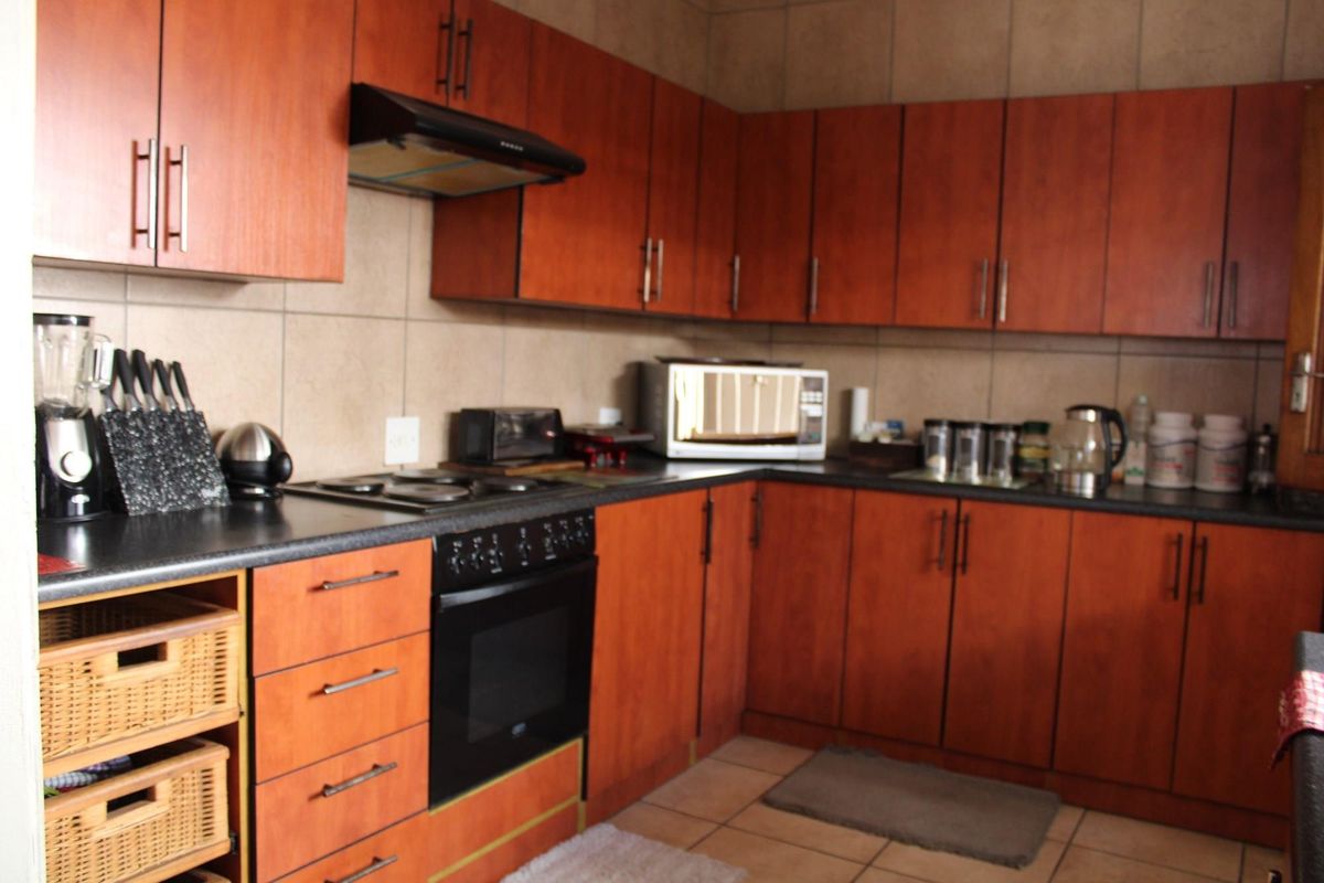 A functional kitchen featuring wood-look laminate cabinetry, dark countertops, built-in oven, electric hob, and tiled splashbacks with neutral floor tiles.