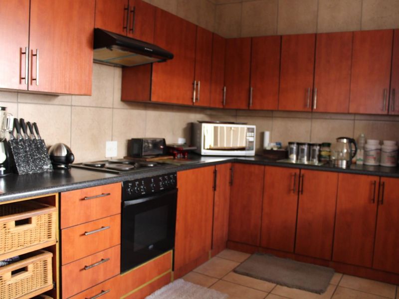 A functional kitchen featuring wood-look laminate cabinetry, dark countertops, built-in oven, electric hob, and tiled splashbacks with neutral floor tiles.