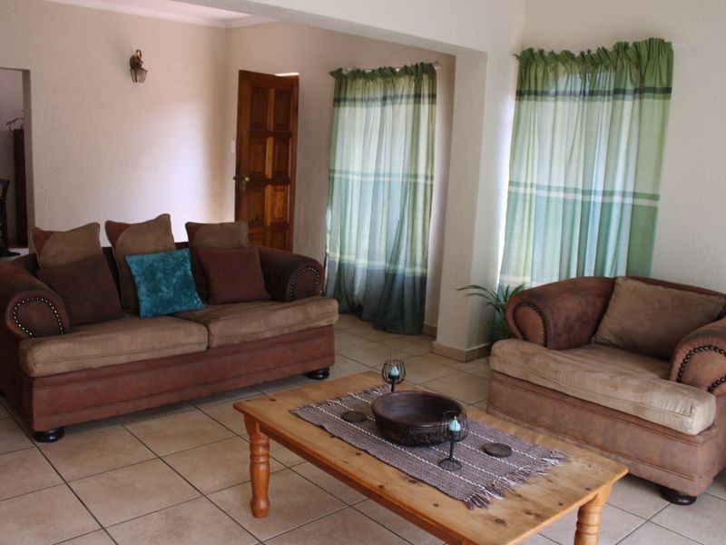 A living room featuring tiled flooring, neutral walls, and access to adjacent rooms through a wooden door.