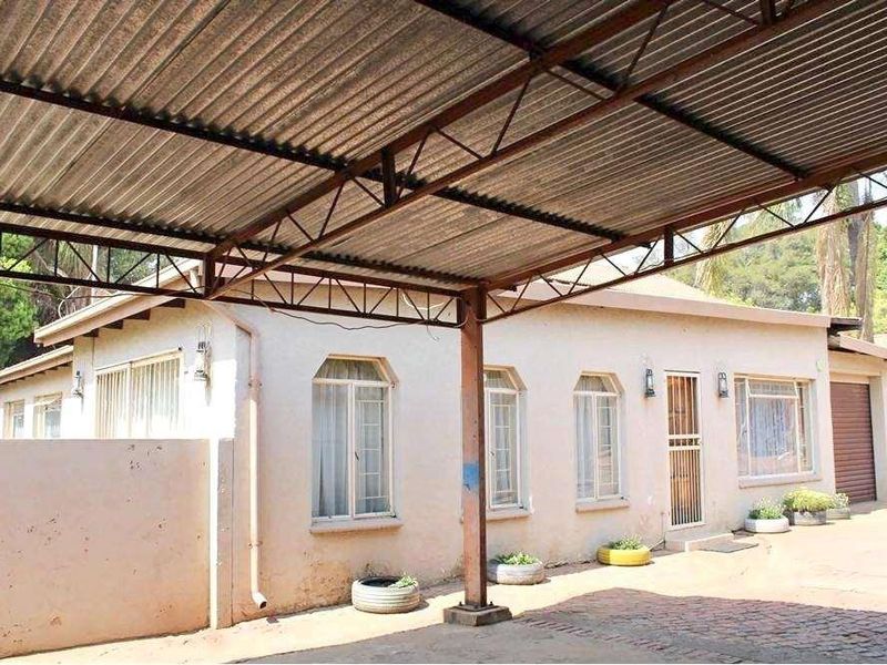 Front exterior view of the house featuring a large corrugated metal carport, paved driveway, and security gate access.