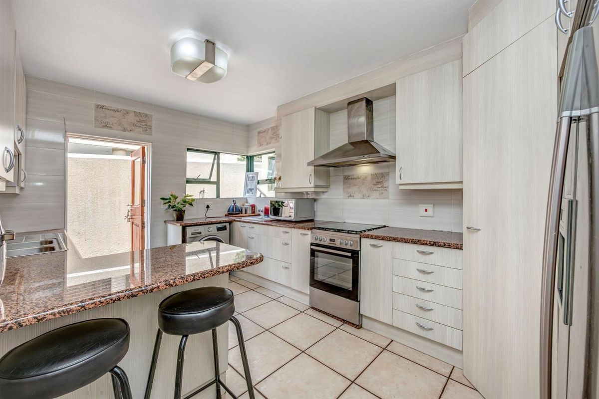 A functional kitchen featuring light wood-grain cabinetry, granite countertops, a breakfast bar, and stainless steel oven with extractor fan, leading to an outdoor area.