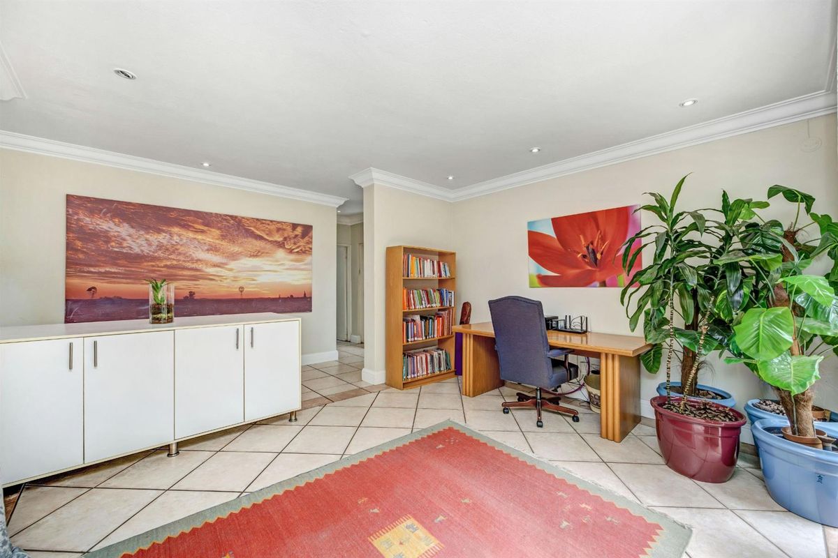 A versatile living space featuring neutral tiled flooring, recessed downlighting, and decorative ceiling cornicing, suitable for use as a home office or lounge area.