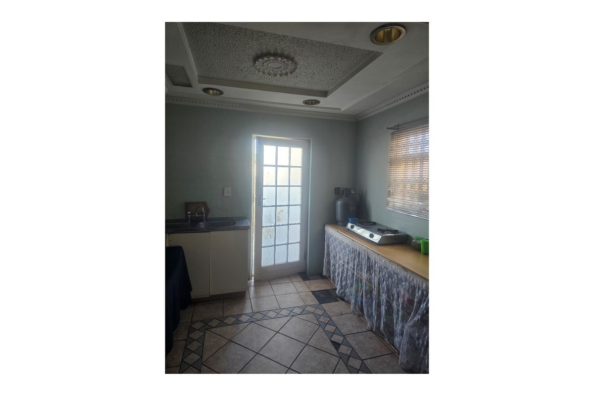 A functional kitchen area featuring tiled flooring, built-in cabinetry, a sink, and a hob, with direct access to the exterior via a glass-paneled door.