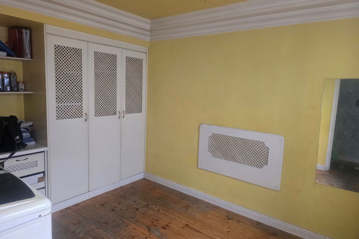Bedroom featuring built-in wardrobes, crown molding, and a radiator cover, with original hardwood flooring and yellow wall finishes.