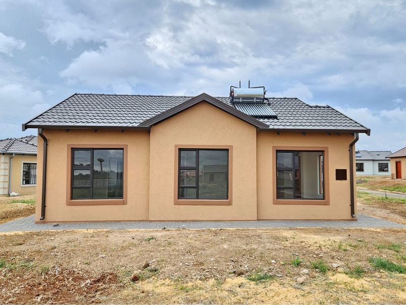 Front elevation of a modern single-story house featuring a tiled roof, solar water heater, and paved perimeter walkway.