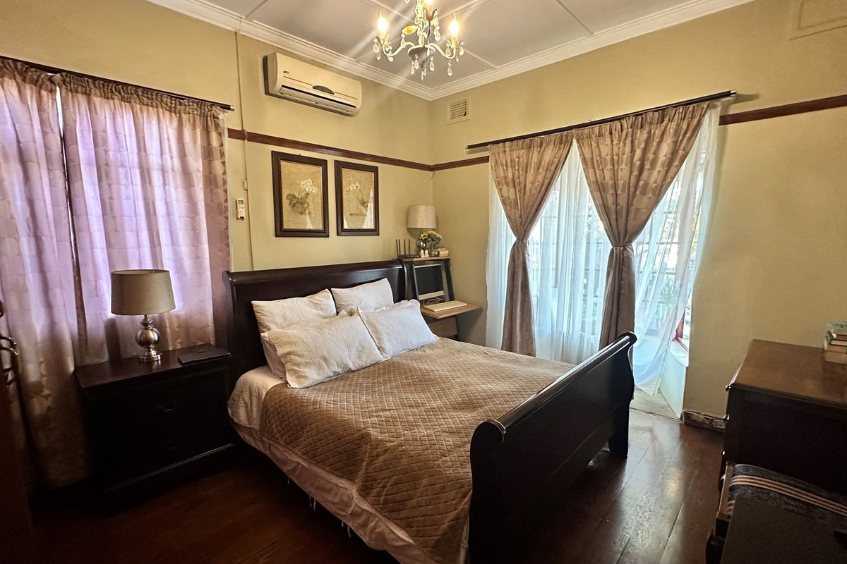 A bedroom featuring polished timber flooring, a wall-mounted air conditioning unit, and direct access to an outdoor area through glass doors.