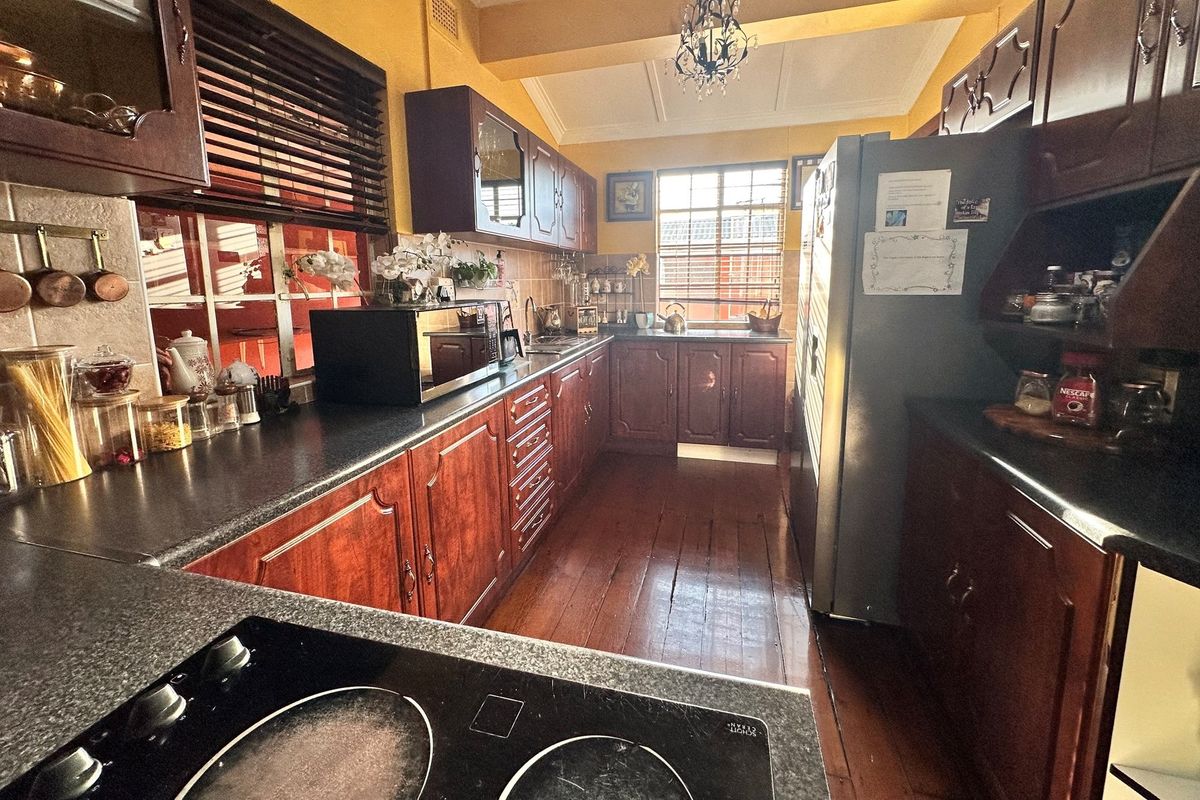A functional kitchen featuring dark timber cabinetry, laminate countertops, a built-in cooktop, and polished timber flooring with natural light from the window.