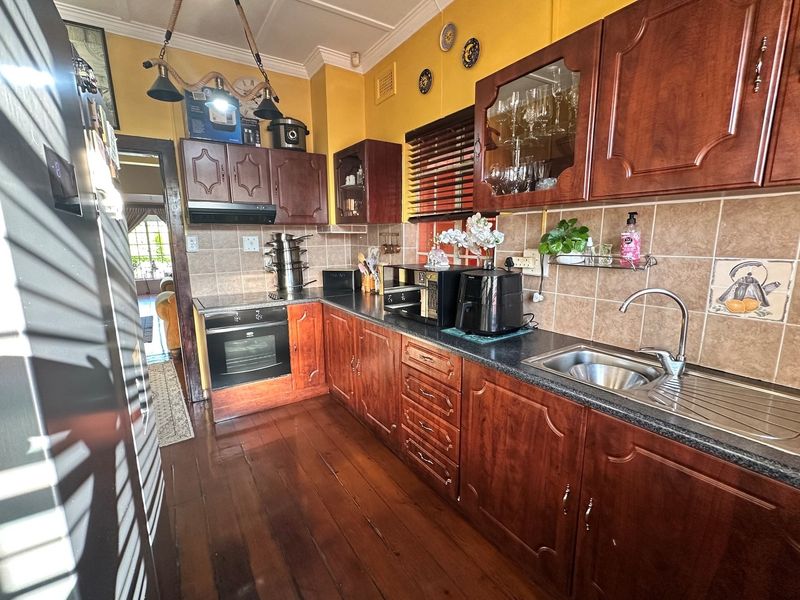 A traditional kitchen featuring dark wood cabinetry, tiled splashbacks, built-in oven, extractor fan, and stainless steel sink with timber flooring.