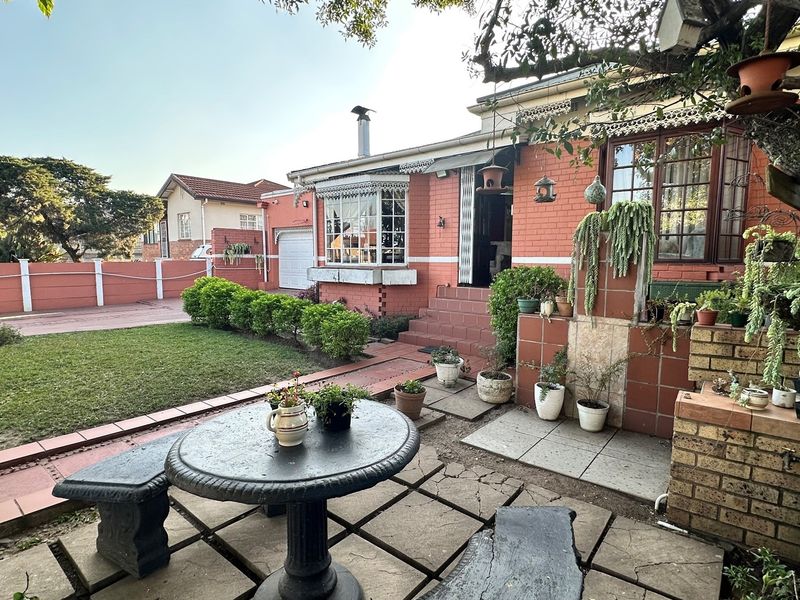 A rear garden area featuring a paved patio, lawn, and brick exterior facade with a bay window and chimney.