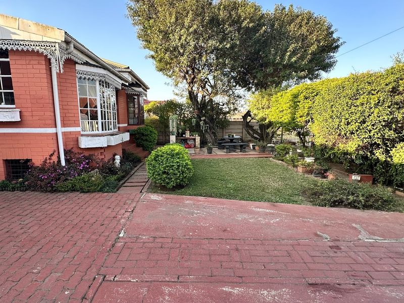 A view of the rear garden featuring a brick-paved area, lawn, mature trees, and a classic red brick exterior facade with decorative trim.