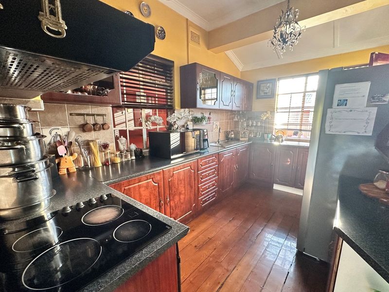 A functional kitchen featuring dark timber cabinetry, laminate countertops, a built-in electric hob, extractor fan, and timber flooring.