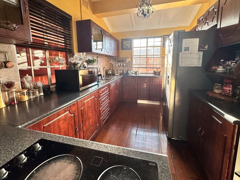 A functional kitchen featuring dark timber cabinetry, laminate countertops, a built-in cooktop, and polished timber flooring with natural light from the window.