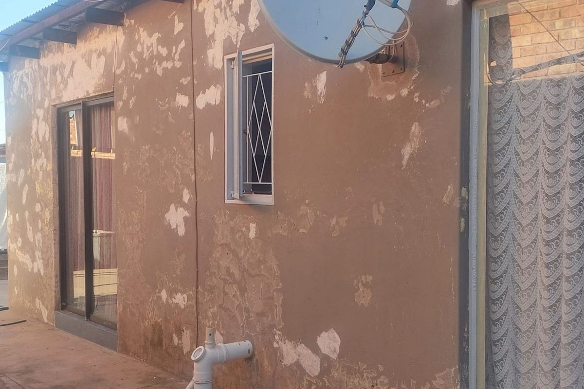 Exterior view of the rear building facade featuring sliding glass doors, a security-grilled window, and visible paint deterioration on the wall surface.