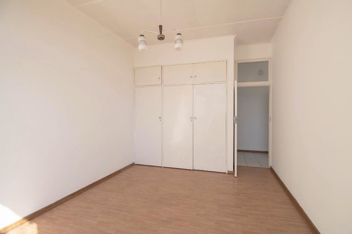A clean, empty bedroom featuring built-in cupboards and light wood-look flooring, offering a neutral space ready for personalization.