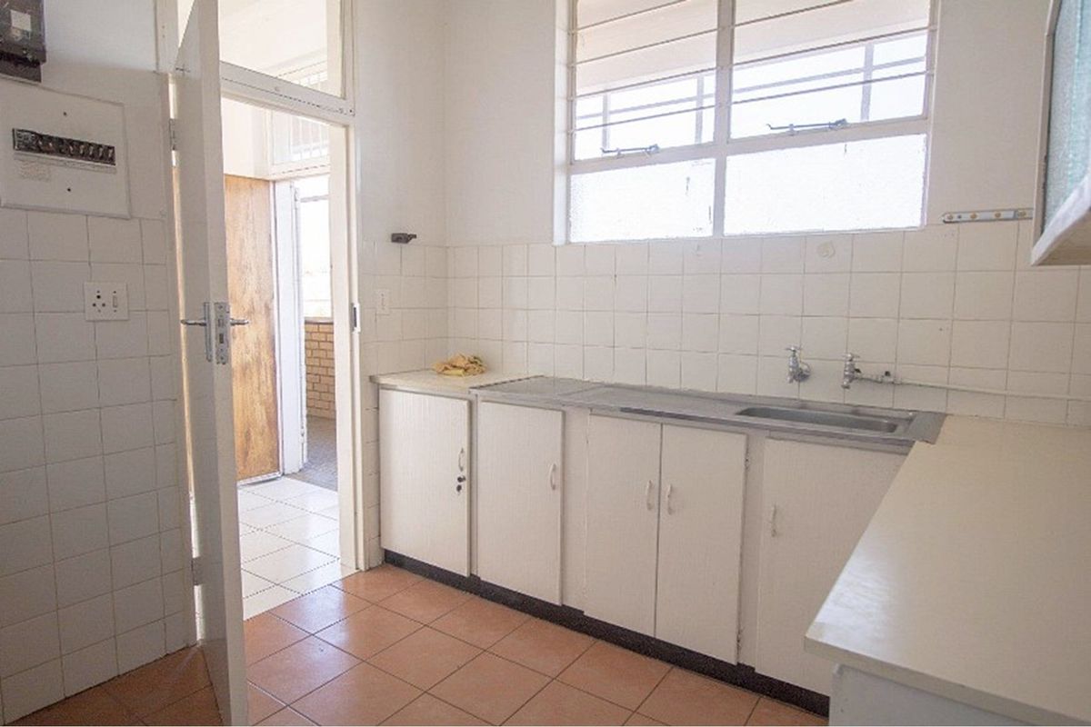 A dated kitchen featuring original cabinetry, tiled splashbacks, and a stainless steel sink, offering a functional space ready for modernization.