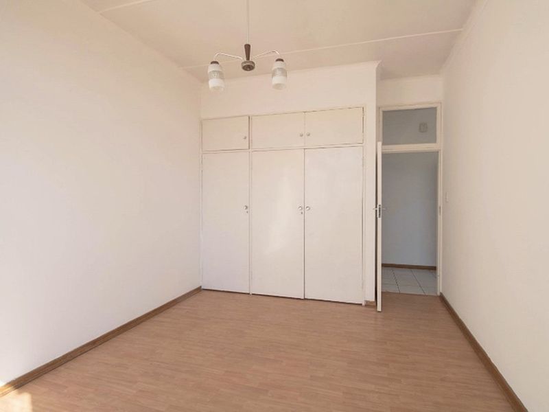 A clean, empty bedroom featuring built-in cupboards and light wood-look flooring, offering a neutral space ready for personalization.