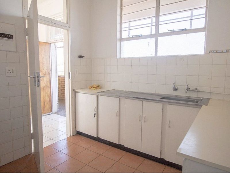 A dated kitchen featuring original cabinetry, tiled splashbacks, and a stainless steel sink, offering a functional space ready for modernization.