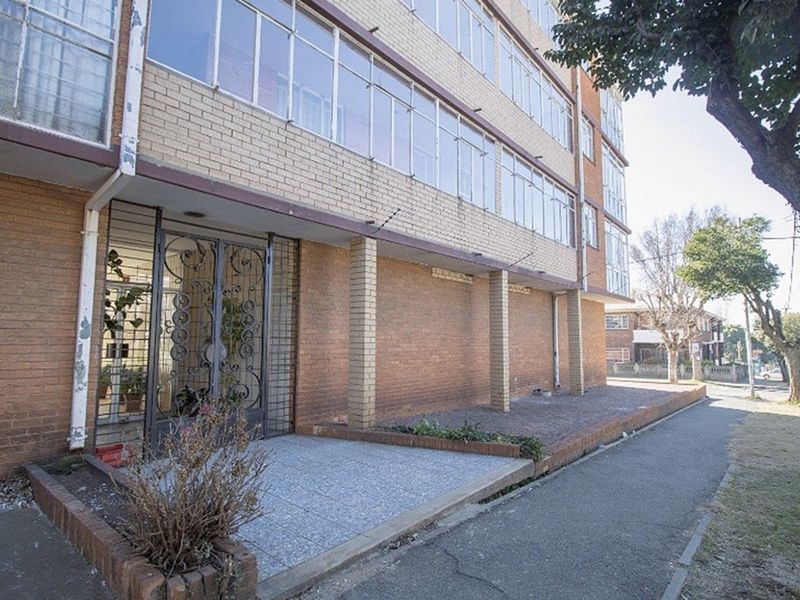 Exterior view of the apartment building facade featuring brick construction, large window banks, and a secure metal entrance gate.