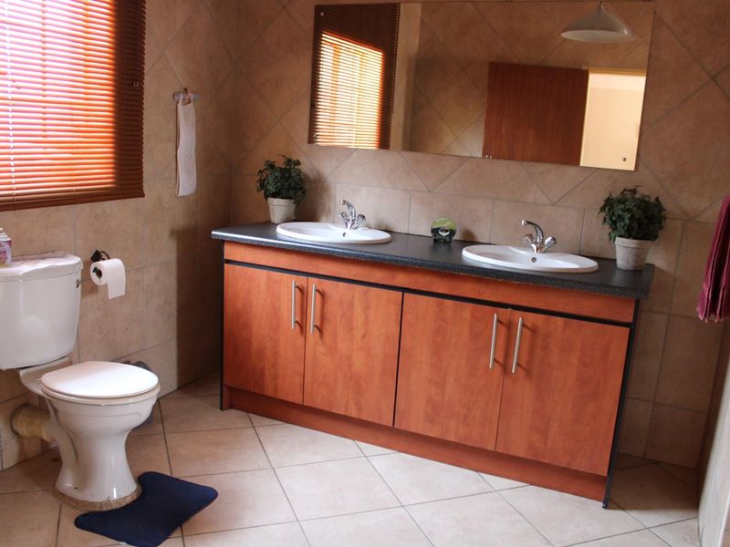 A functional bathroom featuring a double vanity with laminate cabinetry, tiled walls, and ceramic flooring.