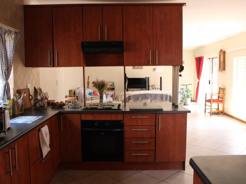 Open-plan kitchen featuring dark wood cabinetry, integrated appliances, and a mirrored splashback, flowing into the adjacent living area with tiled flooring throughout.