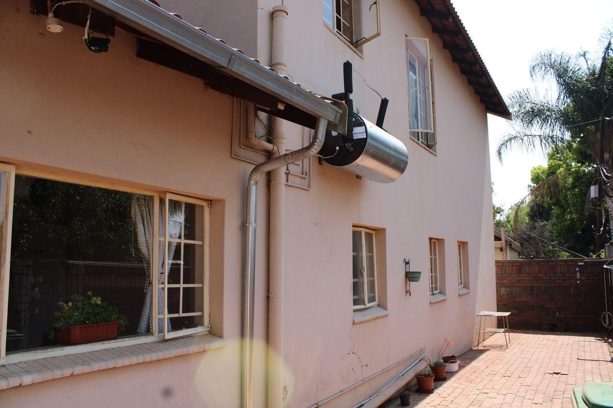 Rear exterior view of the house featuring brick paving, casement windows, and an externally mounted geyser unit on the wall.
