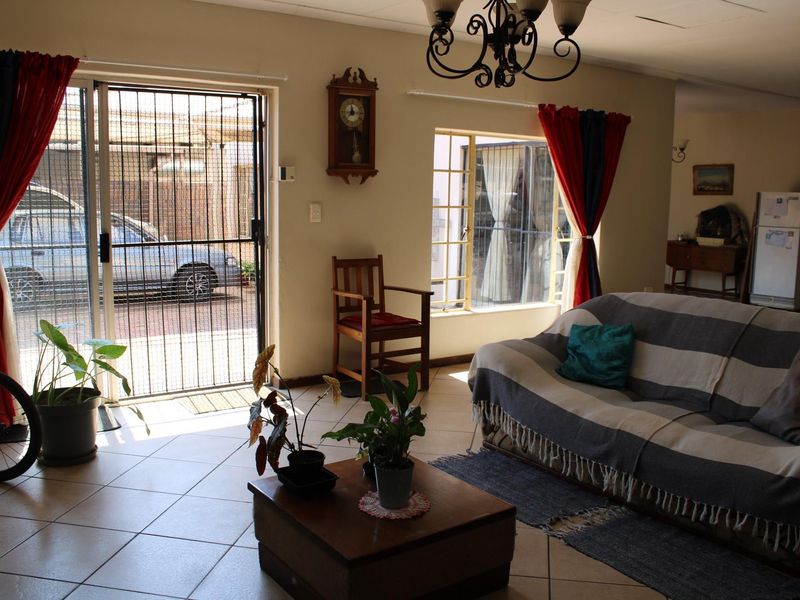 A living room featuring tiled flooring, a sliding door with a security gate, and natural light through windows with burglar bars.
