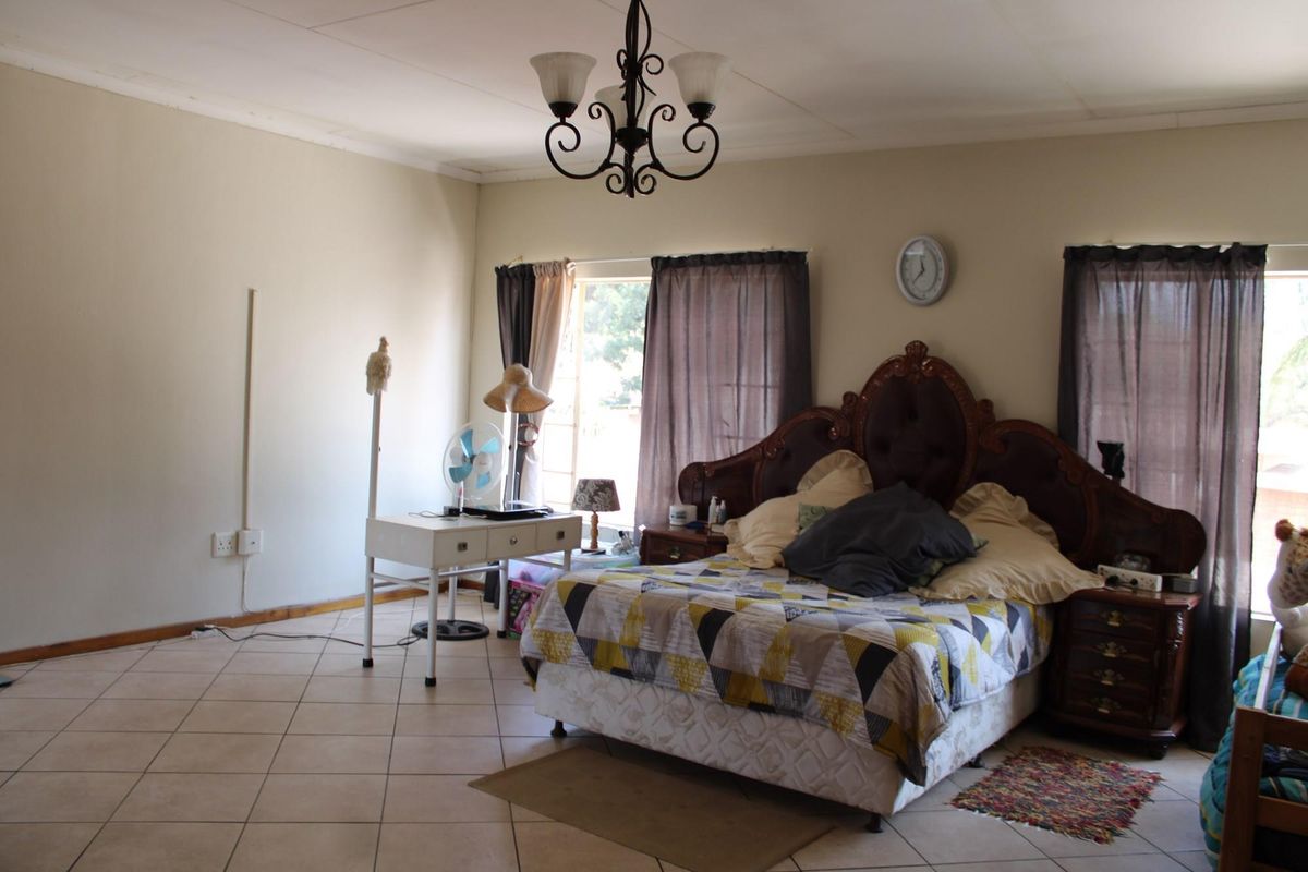 Spacious bedroom featuring tiled flooring, a central chandelier, and coved ceiling details, offering a functional layout with natural light from multiple windows.