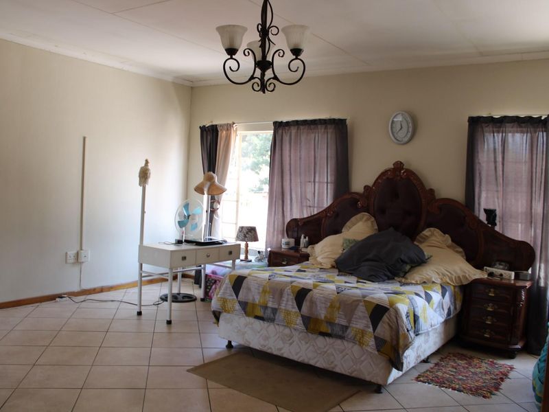 Spacious bedroom featuring tiled flooring, a central chandelier, and coved ceiling details, offering a functional layout with natural light from multiple windows.